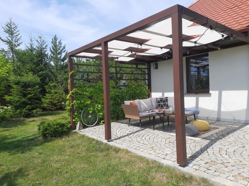 Weißes Sonnenschutz-Seilspannmarkise an einer Holzpergola über der Terrasse mit Gartenmöbeln montiert