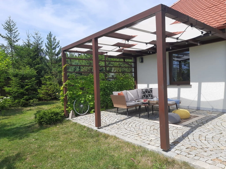 Weißes Sonnenschutz-Seilspannmarkise an einer Holzpergola über der Terrasse mit Gartenmöbeln montiert