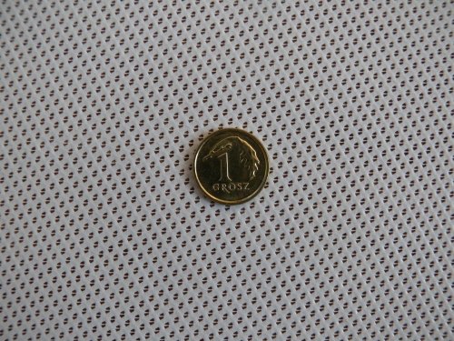 Polish 1 grosz coin centered on a textured white sunshade sail fabric.