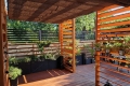 Store romain solaire marron en HDPE monté sur une pergola en bois au-dessus d'une terrasse élégante avec des plantes