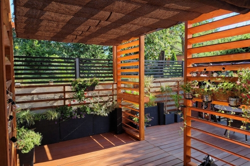 Braunes Raffrollo HDPE-Sonnenschutz montiert an einer Holzpergola über einer stilvollen Terrasse mit Pflanzen