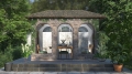 Transparent custom patio tarp with archway print on an outdoor stone gazebo with a dining table and green chairs.