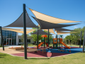 Custom UV-resistant sun shade sails installed over a modern playground with colorful climbing frames and slides.