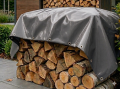 Durable grey waterproof tarp covering a large stack of chopped firewood outdoors to keep logs dry for a fireplace