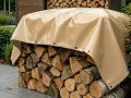 Durable beige waterproof tarp with metal grommets covering a stacked woodpile of firewood logs outdoors