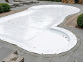 Copertura bianca per piscina di forma irregolare su misura, fissata con corde alla terrazza in pietra
