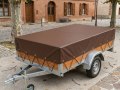 Custom brown waterproof trailer cover with reinforced eyelets on a wooden utility trailer parked on a cobblestone street
