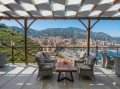 Two-color waterproof pergola shade sail over an elegant terrace lounge overlooking a Mediterranean harbor and city.