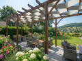 Two-color waterproof pergola shade sails woven through a wooden garden pergola with outdoor seating and flowers