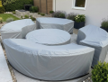 Custom-made gray protective covers on a curved outdoor sofa set with a round table in a patio garden.