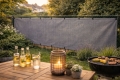 Grijs HDPE-hekwerkzeil voor windbescherming en schaduw, gemonteerd op tuinhek bij tafel en barbecue