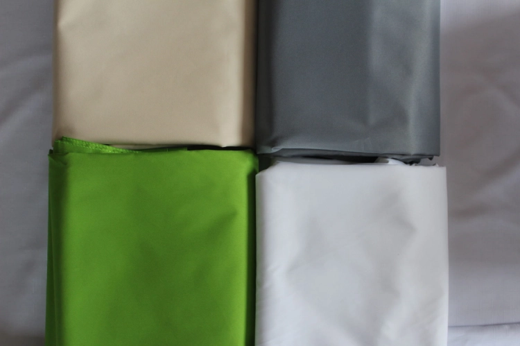 Folded waterproof pergola fabric swatches in cream, gray, lime green, and white for premium sun shade protection