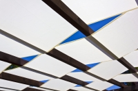 White waterproof pergola shade sail strips woven through dark wooden beams against a clear blue sky.