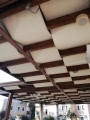 Toldo de pérgola premium beige impermeable instalado bajo una estructura de madera de terraza como protección solar