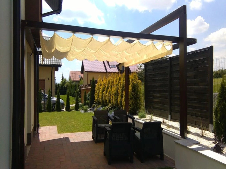 Retractable cream Roman pergola shade canopy over a modern dark wood patio frame with outdoor seating and garden view