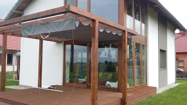 Grey waterproof Roman shade on a 3x4 meter wooden terrace pergola attached to a modern house with large windows.