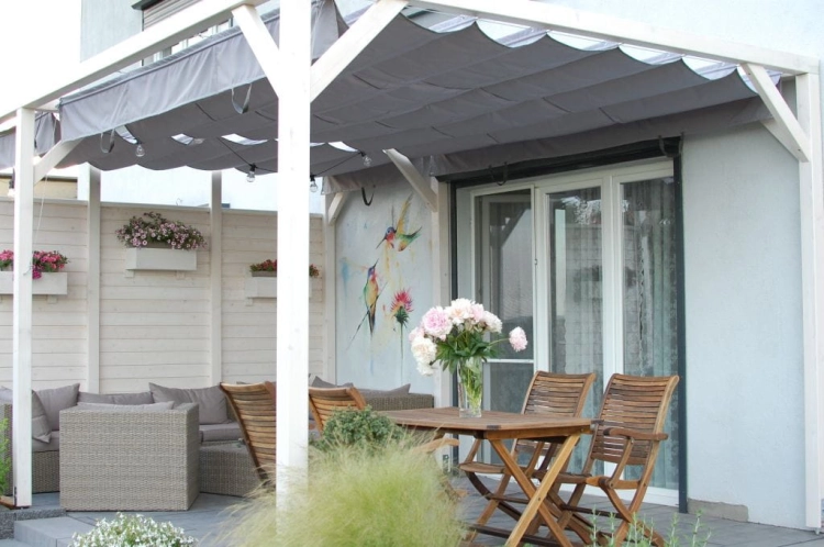 Grey waterproof premium roman sunshade sail installed on a white wooden pergola over a garden patio set