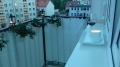 White custom-sized balcony privacy screen on a railing with flower pots, a glass of wine, and a candle at dusk