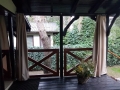Cortinas de terraza beige instaladas en una terraza de madera negra con vistas al jardín y la vegetación