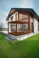 Wit terrasgordijn op maat opgehangen aan een moderne houten pergola met ligstoelen voor het huis