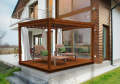White tailored outdoor curtain for a wooden terrace pergola with lounge chairs next to a modern house.