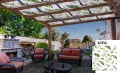 Wasserdichte Pavillonbahn mit Pflanzendruck auf einer Holzpergola über einer Terrasse mit Loungemöbeln