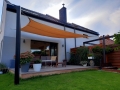 Maßgefertigtes orangefarbenes HDPE-Sonnensegel über einer Terrasse mit modernen Gartenmöbeln montiert