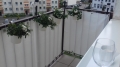 White privacy screen cover for balcony railing with hanging flower pots and a view of apartment buildings.