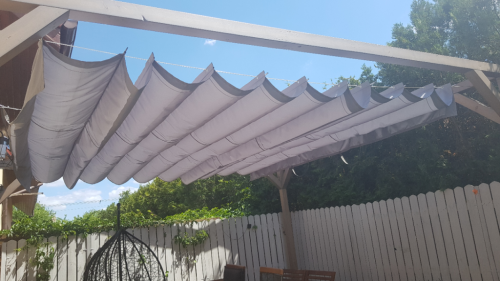 Gray waterproof premium roman sunshade sail installed on a wooden pergola in a backyard garden terrace.