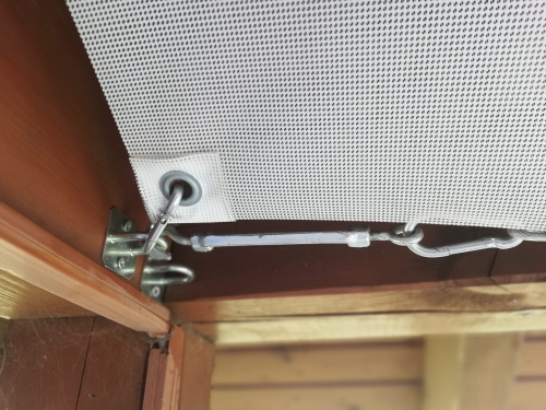 Retractable sun shade sail corner attachment with metal turnbuckle and carabiner hooked to a wooden frame