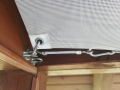 Close-up of a retractable sun shade sail hardware with a turnbuckle and carabiner hooked to a wooden frame turnbuckle
