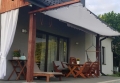 White retractable shade sail covering a patio with wooden furniture, string lights, and a hanging chair