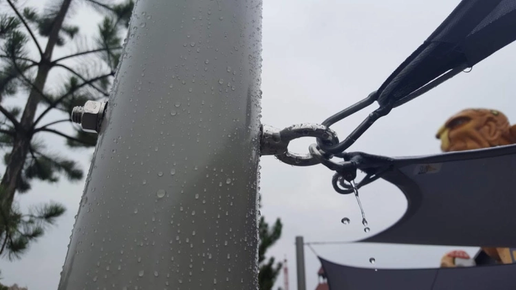 Close-up of a stainless steel mounting eye bolt securing a waterproof square sun shade sail to a durable metal pole