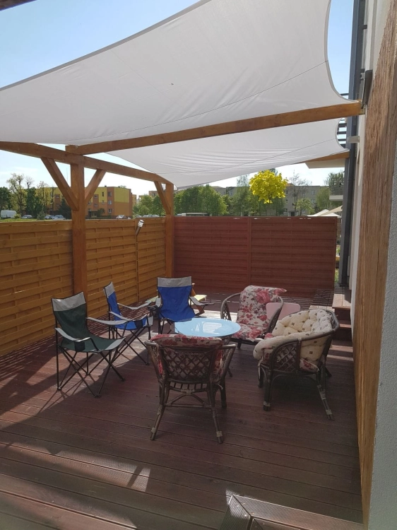 Wasserdichtes quadratisches Sonnensegel 4x4 m montiert über einer Terrasse mit Loungemöbeln am Haus