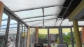 Wit schaduwdoek gemonteerd op metalen frame onder het glazen dak van een wintertuin
