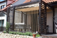 Retractable Roman shade mounted on a wooden pergola over a patio, providing shade and sun protection