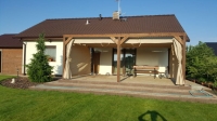 Beige waterproof garden curtains hung on a custom wooden pergola attached to a modern house with a patio.