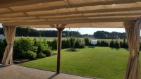 Custom waterproof garden curtains tied to the sides of a gazebo overlooking a lush backyard lawn and trees