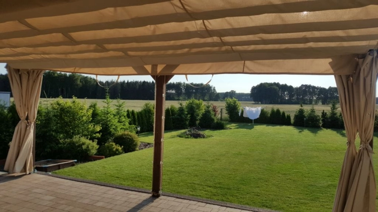 Custom waterproof garden curtains tied to the sides of a gazebo overlooking a lush backyard lawn and trees