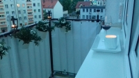 White privacy balcony screen installed on a railing with flower pots, a glass of wine, and a candle on a sill.